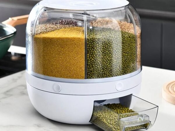 A white 6-grid rotating food dispenser on a kitchen counter, with different grains like rice and beans visible in each compartment.